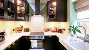 A modern kitchen with dark cabinets, a central island, and a built-in oven. - Perfect Booking Steps From Brixton Station (London)