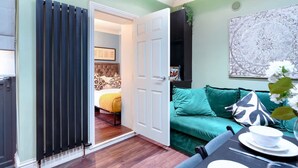 A room with a bed, a green sofa, a dining table with a white bowl, and a radiator. - Perfect Booking Steps From Brixton Station (London)