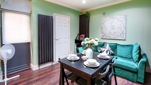 A dining area with a table set for four, a fan, a window with blinds, a door, and a green sofa. - Perfect Booking Steps From Brixton Station (London)