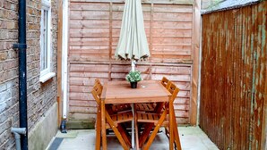 A wooden table with chairs and an umbrella in a fenced outdoor area. - Perfect Booking Steps From Brixton Station (London)