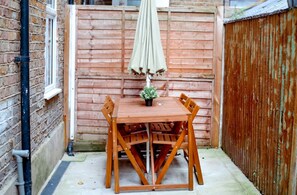 A wooden table with chairs and an umbrella in a fenced outdoor area. - Perfect Booking Steps From Brixton Station (London)