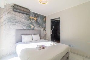 A modern hotel room with a marble-patterned wall, a large bed with white linens, and a ceiling-mounted air conditioner. - Beautiful Apartment With Pool Near Monaco (Beausoleil)