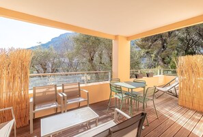 A balcony with wooden flooring, metal chairs, a glass table, and a view of trees and mountains. - Beautiful Apartment With Pool Near Monaco (Beausoleil)
