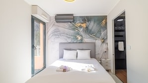 Un dormitorio moderno con un mural de mármol, una cama grande con ropa de cama blanca, una mesita de noche y un vestidor.