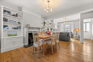 Een ruime woonkamer met een open haard, een eettafel met stoelen en een groot raam.