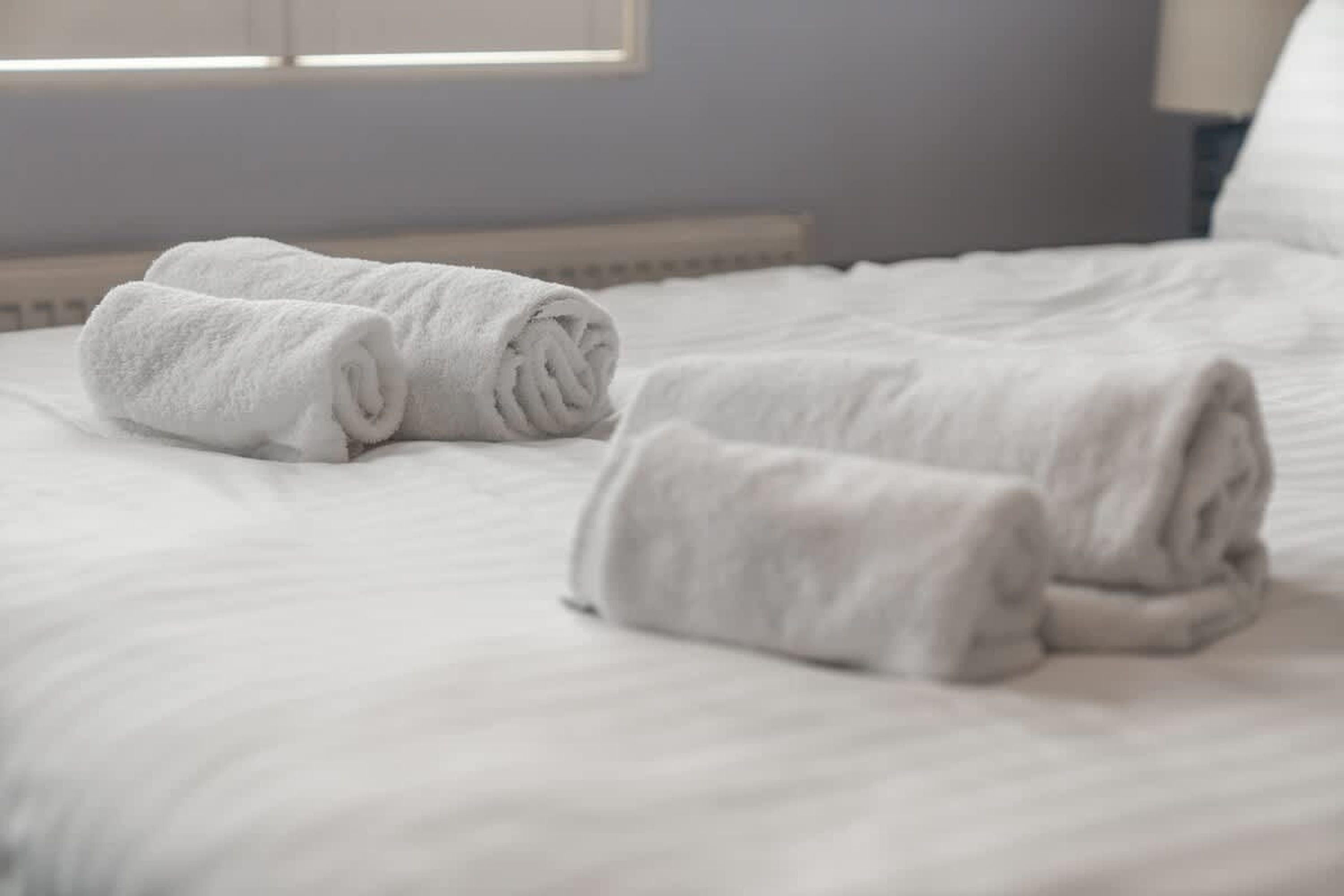 A neatly made bed with rolled white towels.