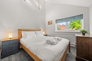 Quarto com cama de madeira, mesa de cabeceira, cômoda, janela com vista e radiador.