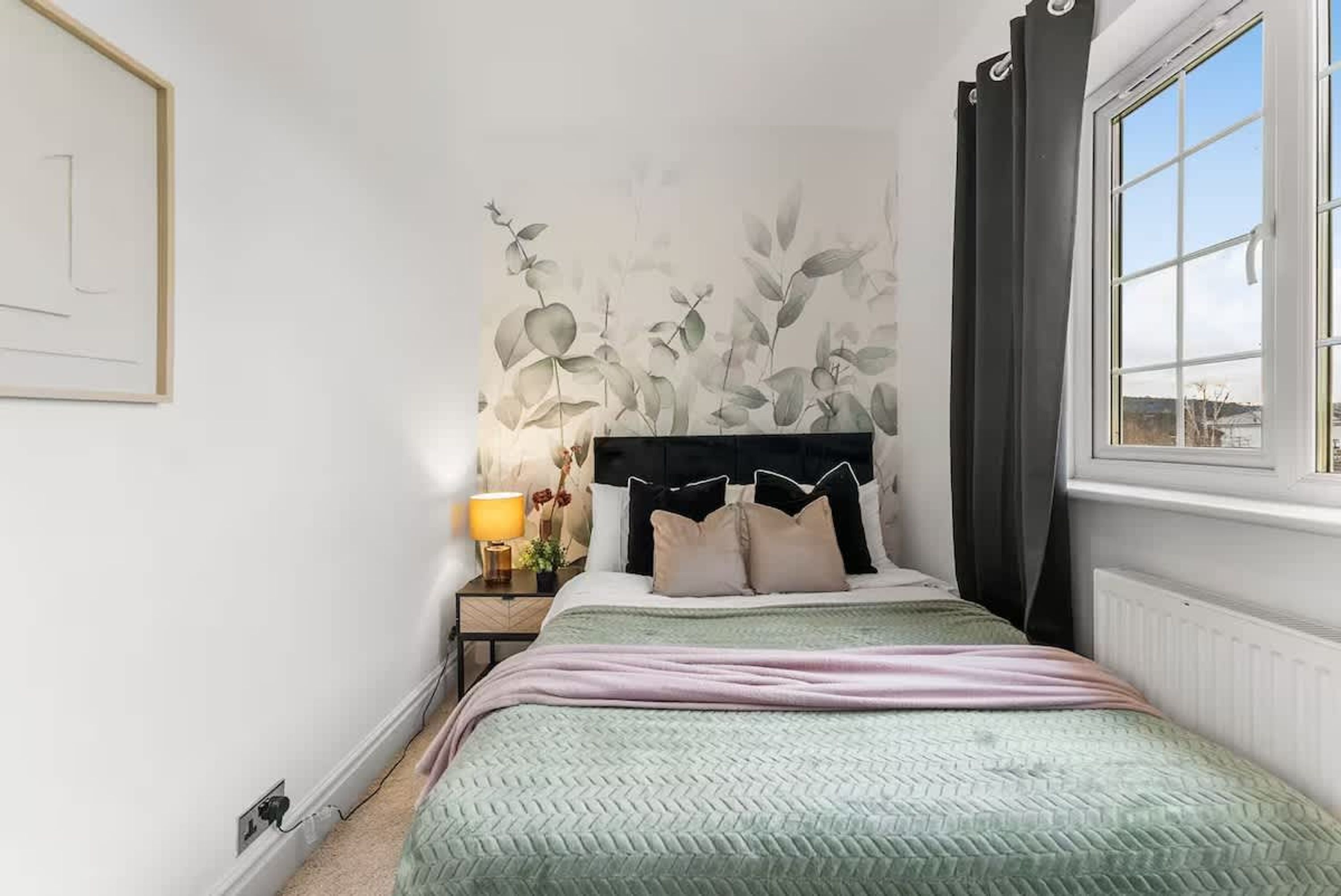 Un dormitorio con cama, mesita de noche, lámpara y ventana con cortinas.