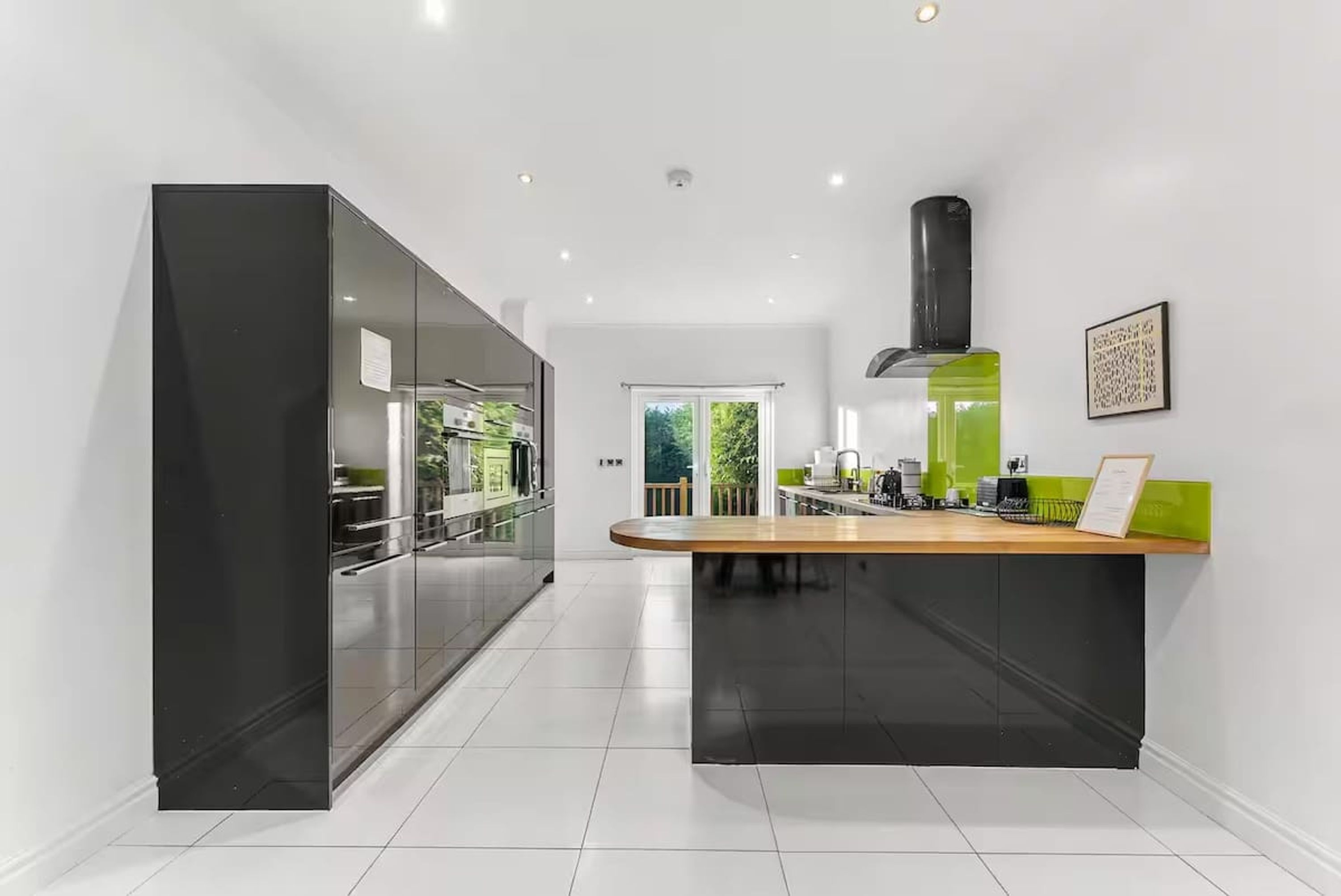 A modern kitchen with a central island, black cabinetry, and a green accent wall.