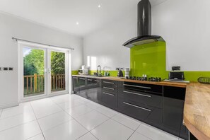 Eine moderne Küche mit schwarzen Schränken, einer grünen Akzentwand, einem großen Fenster und einer Glastür, die auf einen Balkon führt.
