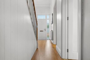A hallway with white walls, a wooden floor, and a door at the end. - Perfect Booking 4 Bed Home in Cheltenham (Cheltenham)