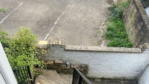 Una escalera que lleva a la entrada de un edificio, con barandilla metálica y pared de ladrillo.
