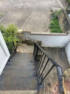 Eine Treppe führt zu einem Gebäudeeingang mit einem Metallgeländer und einer Backsteinmauer.
