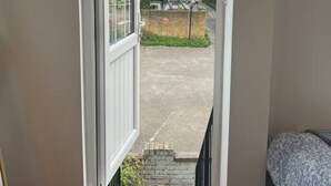 Puerta abierta que da a un balcón con vistas a una zona residencial y un muro de ladrillo.