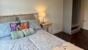 Un dormitorio con cama, almohadas, una mesita de noche con lámpara y un armario.