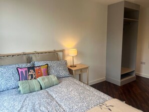 Ein Schlafzimmer mit Bett, Kissen, einem Nachttisch mit Lampe und einem Kleiderschrank.