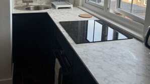 Cocina con salpicadero de mármol, encimera negra, ventana y vista a edificios.