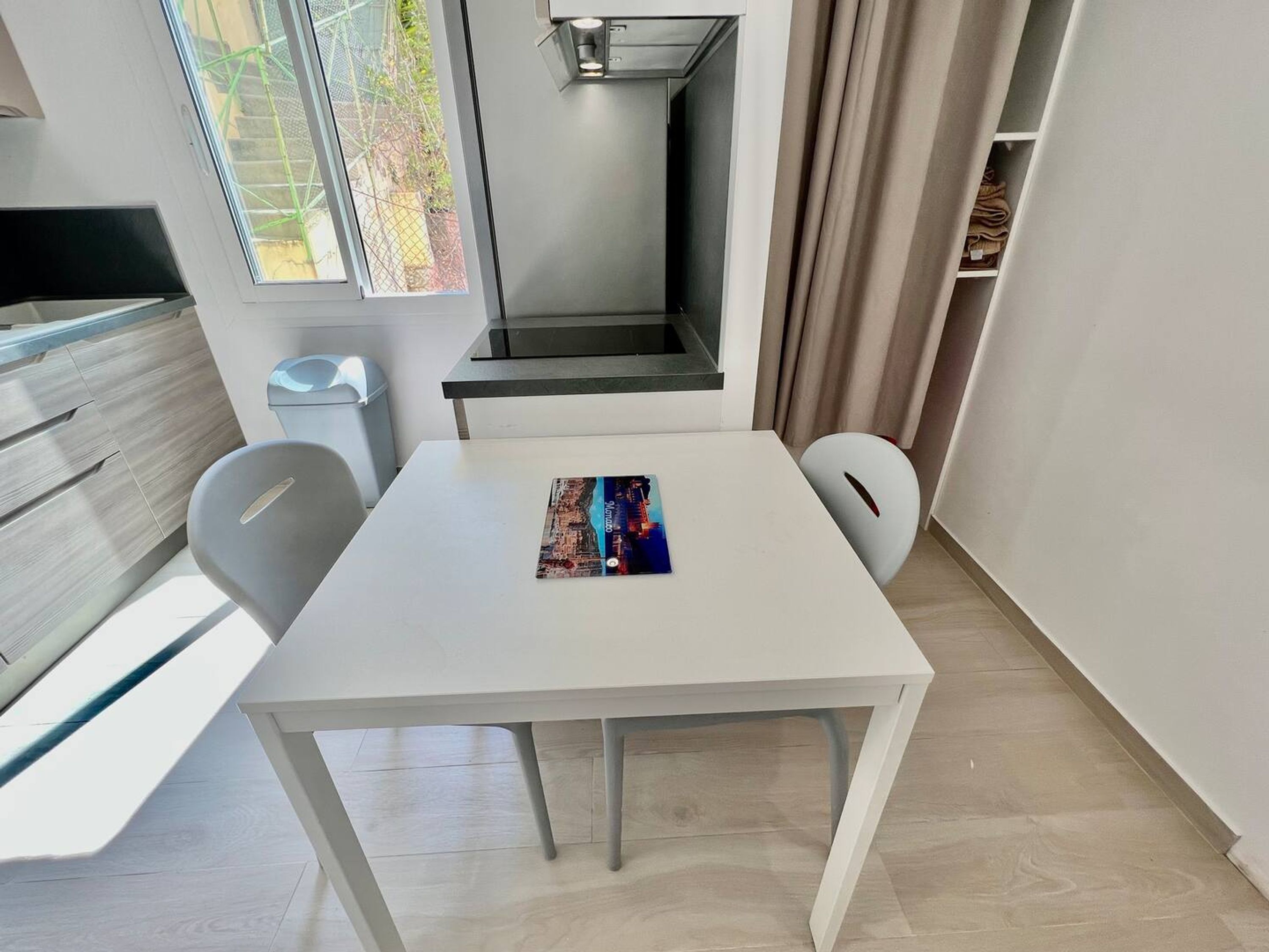 Una cocina moderna con una mesa blanca, sillas y una ventana con vistas a un jardín.