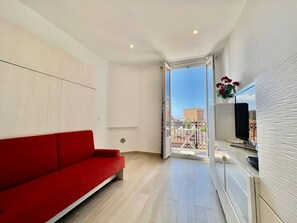 Een moderne woonkamer met een rode bank, een televisie en stadszicht door een glazen deur.