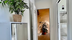Un pasillo con una planta en maceta, una puerta blanca y un baño visible a través de una puerta abierta.
