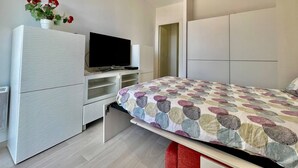 Un dormitorio con una cama, televisión sobre un mueble, armario y una mesita con una planta.
