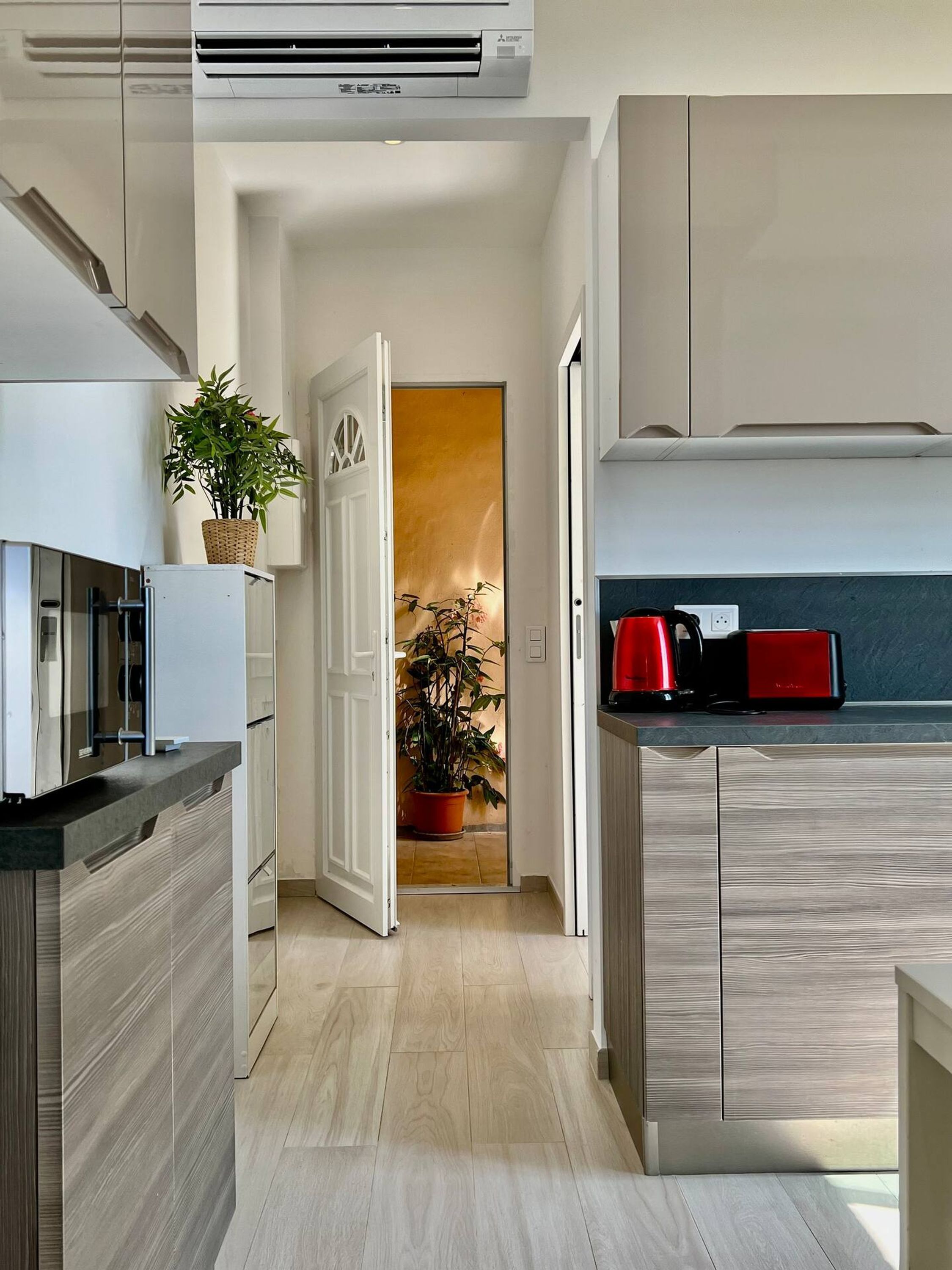 A modern kitchen with a built-in air conditioner, a potted plant, and a red coffee maker on the counter.