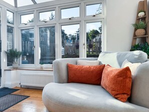 A living room with a sofa, a bay window with multiple panes, a radiator, and a wooden floor.