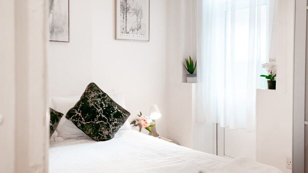 Une chambre à coucher comprenant un lit, une table de chevet, une lampe, une fenêtre avec des rideaux et des œuvres d’art murales.
