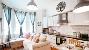 Une cuisine moderne avec des meubles blancs, une table à manger dressée avec des assiettes et des verres, et un canapé dans l’espace salon.