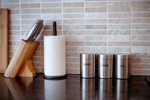 A kitchen counter with a paper towel holder, a knife block, and stainless steel containers labeled 'COFFEE,' 'SUGAR,' and 'TEA.' - Perfect Booking 1 Minute Walk To Brixton Station (London)