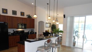 A modern kitchen with wooden cabinets, a central island with bar stools, pendant lighting, and a view to a balcony. - Villa Corthouts Luxury Home Close to Bike Trail (Inverness)