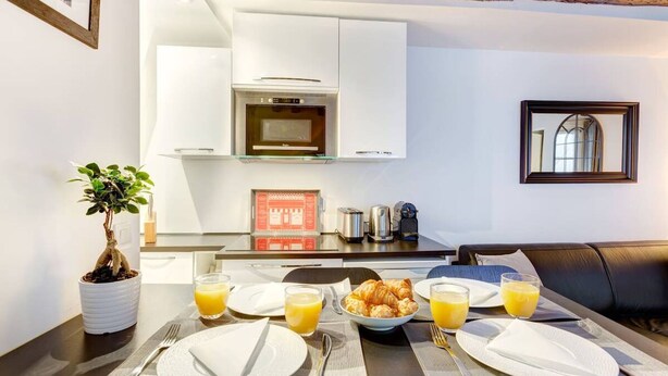 Ein Frühstücksangebot mit Croissants, Orangensaft und einer Kaffeemaschine in einer modernen Küche mit weißen Schränken und Holzbalkendecke.