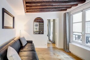 A room with a black leather sofa, a wooden ceiling, a large window with a view, and a door leading to another room. - Chic Marais Retreat Steps to Cafes Notre Dame (Paris)