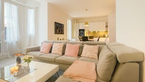 A modern living room with a beige sofa, a glass coffee table, and a kitchen in the background. - Stylish 3-bedroom Gem Steps From Monaco Spacious (Beausoleil)