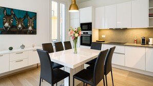 A modern kitchen with white cabinets, a dining table with chairs, a painting of donkeys, and a vase with flowers. - Stylish 3-bedroom Gem Steps From Monaco Spacious (Beausoleil)