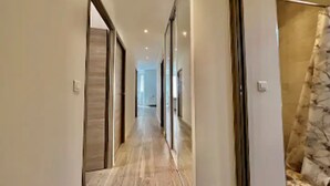 A hallway with a wooden floor, a glass door on the right, and a view into another room. - Stylish 3-bedroom Gem Steps From Monaco Spacious (Beausoleil)