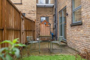 A small backyard with a wooden fence, a metal table, and two metal chairs. - Spacious 2-bed Flat With Outdoor Patio (London)