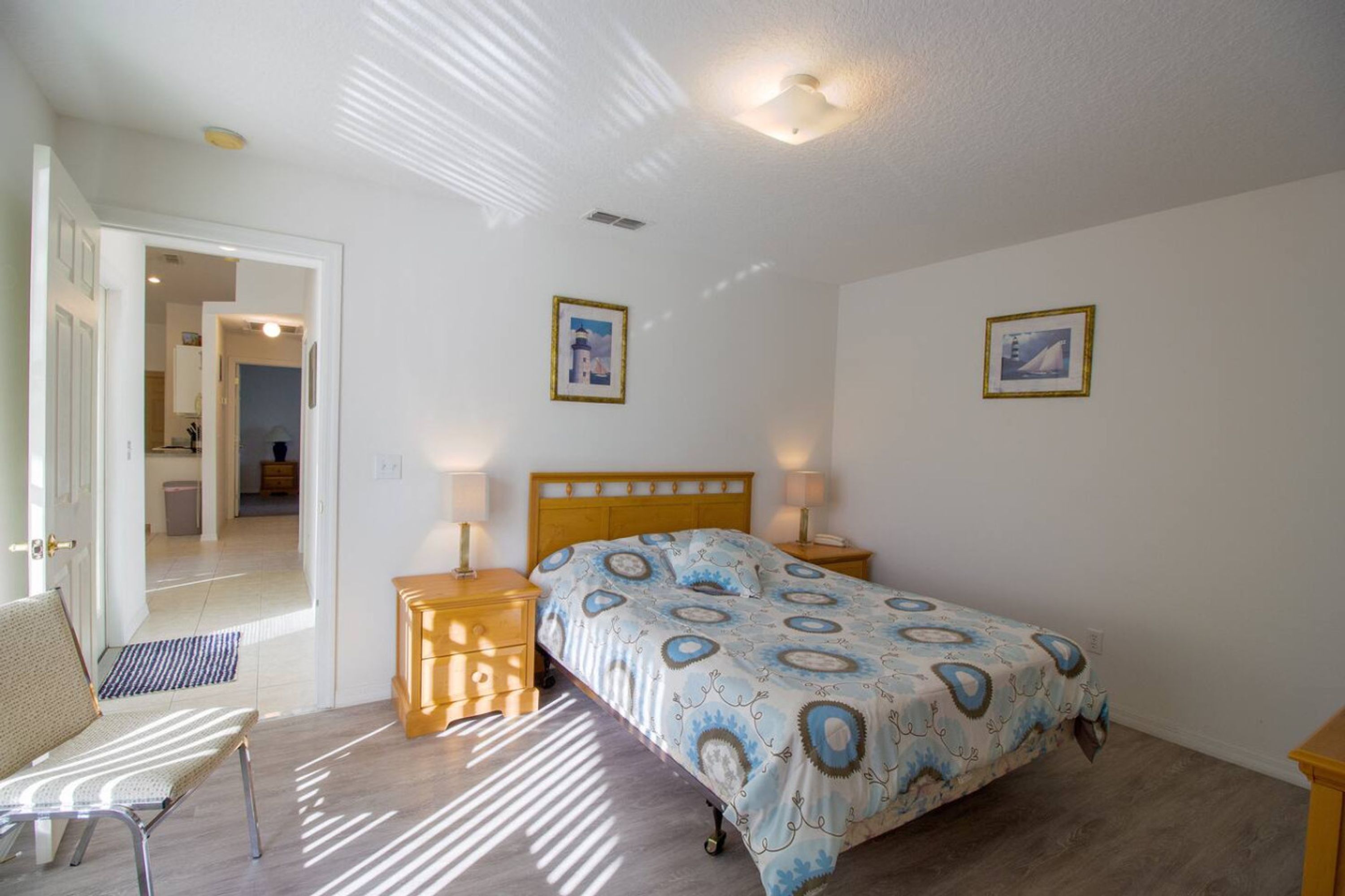 A bedroom with a bed, two bedside tables, a chair, and a door leading to another room.
