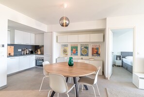 A modern kitchen with white cabinets, a dining table with chairs, and a hanging light fixture. - Superb new 2-room Apartment -parking Border Monac (Beausoleil)