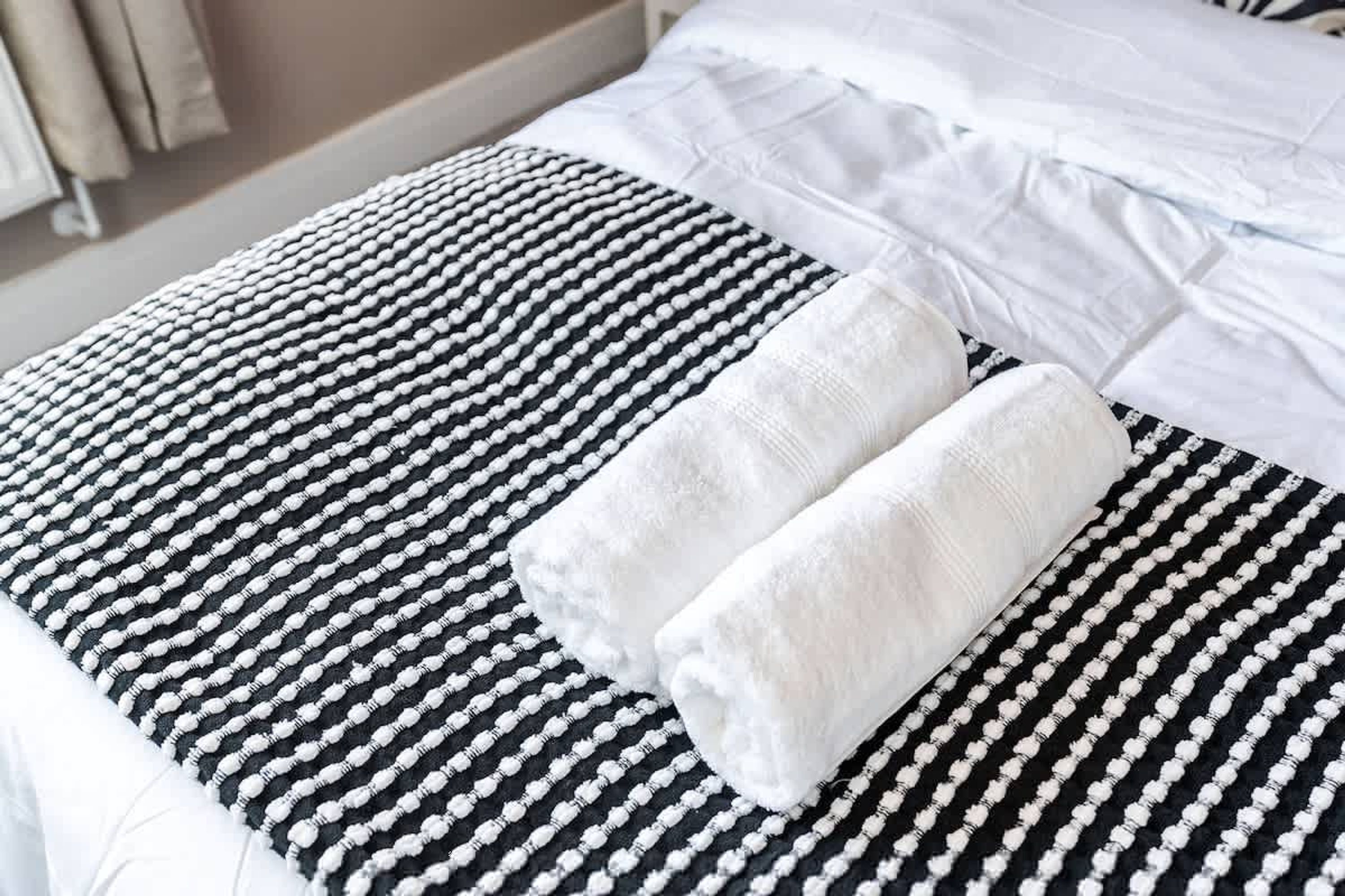 A bed with a black and white striped bedspread, two rolled white towels, and white pillows.