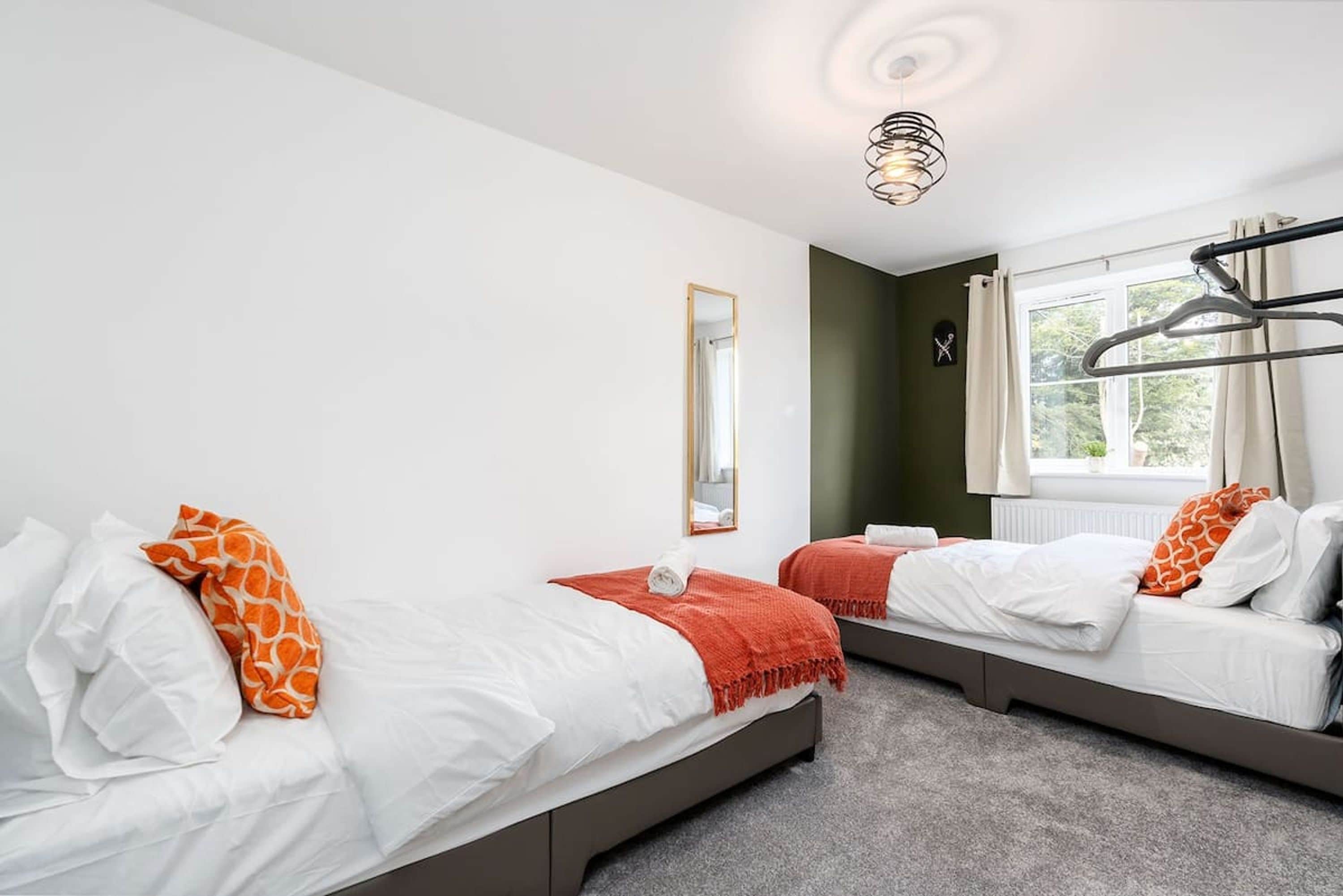 Hotellihuone, jossa on kaksi sänkyä, peili, ikkuna verhoilla ja kattovalaisin.