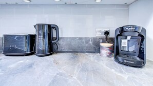 Una cuina amb cafetera, torradora i bullidor damunt un taulell de marbre.