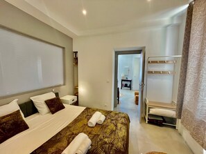 A hotel room with a bed, a bedside table, a nightstand, a wardrobe, and a bathroom visible through an open door. - Apartment Monaco Beach Grimaldi Forum (Beausoleil)