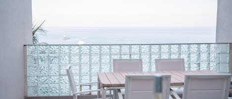 A balcony with a view of the sea, a table with chairs, and a bottle of wine.