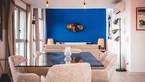 Een eethoek met een glazen tafel, vier stoelen, een blauwe accentmuur en een vloerlamp.