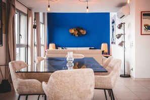 Ein Essbereich mit einem Glastisch, vier Stühlen, einer blauen Akzentwand und einer Stehlampe.