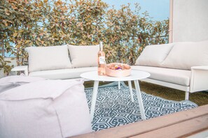 Ein weißes Sofa mit Kissen, ein runder weißer Tisch und ein Teppich mit Muster auf einer Terrasse.