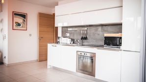 Een moderne keuken met witte kastjes, een ingebouwde oven, een magnetron en een houten deur.