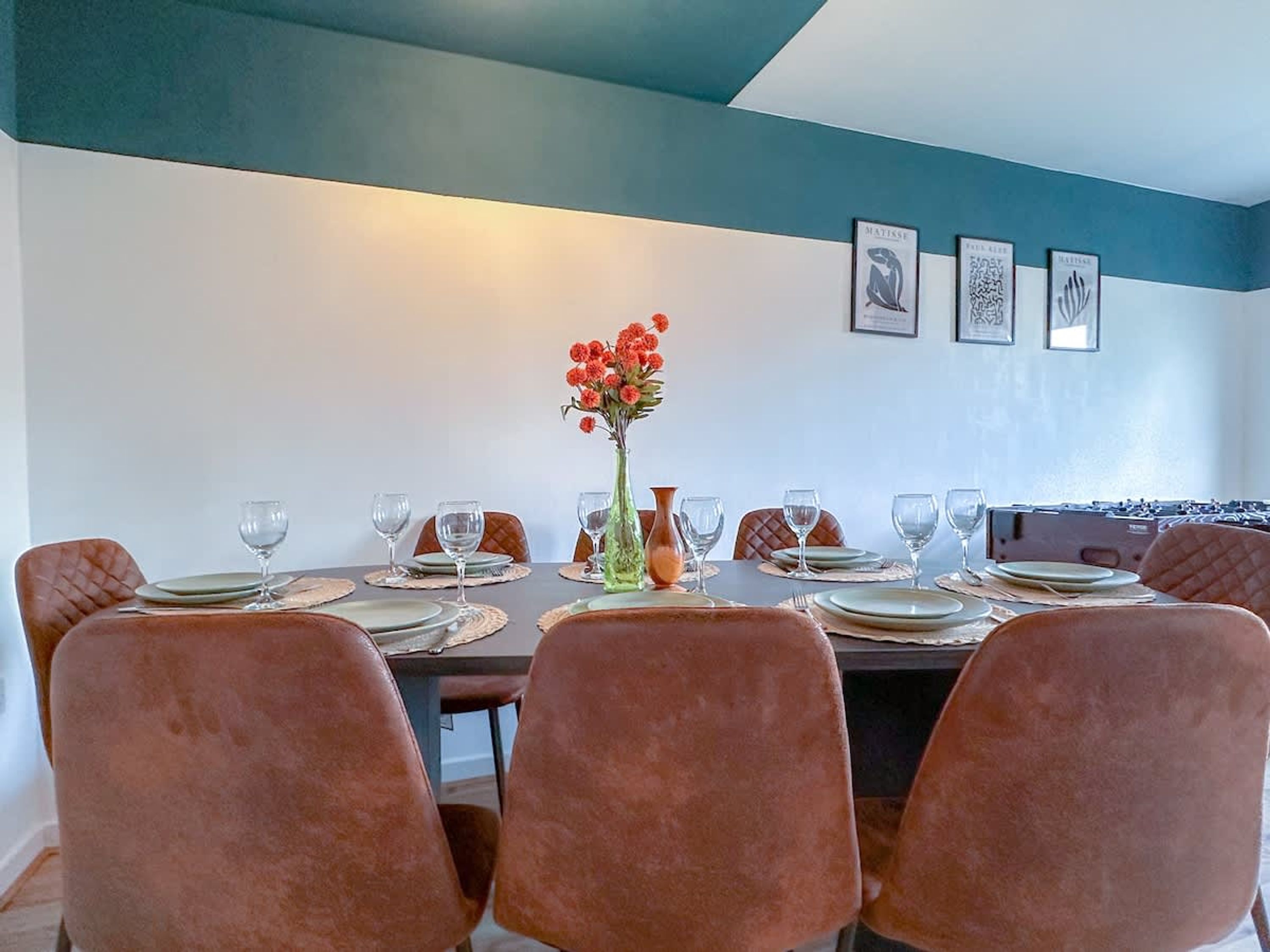 A dining area with a table set for six, six chairs, and a vase of flowers.