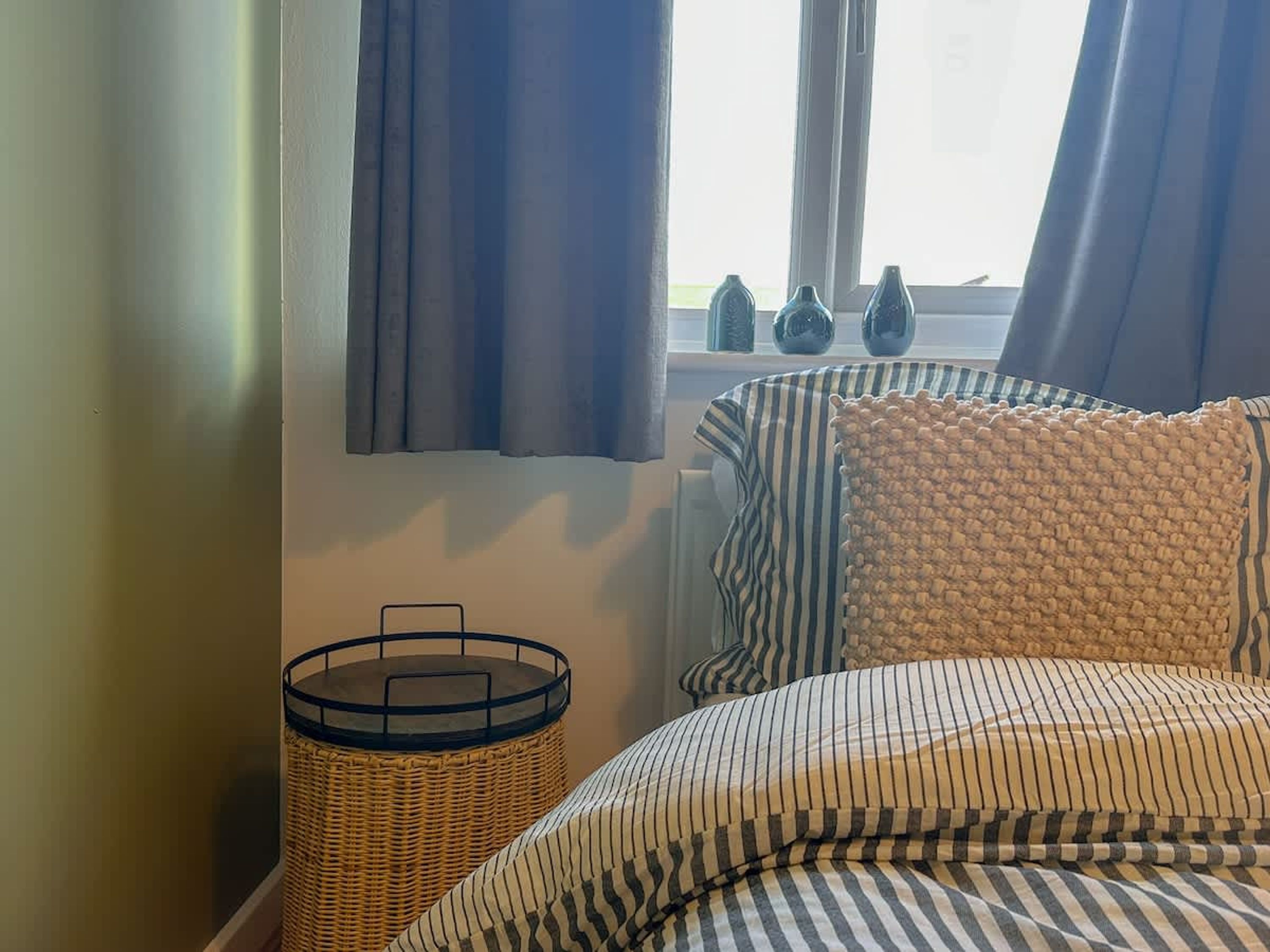 A bedroom with a bed, a wicker basket, and a window with curtains.